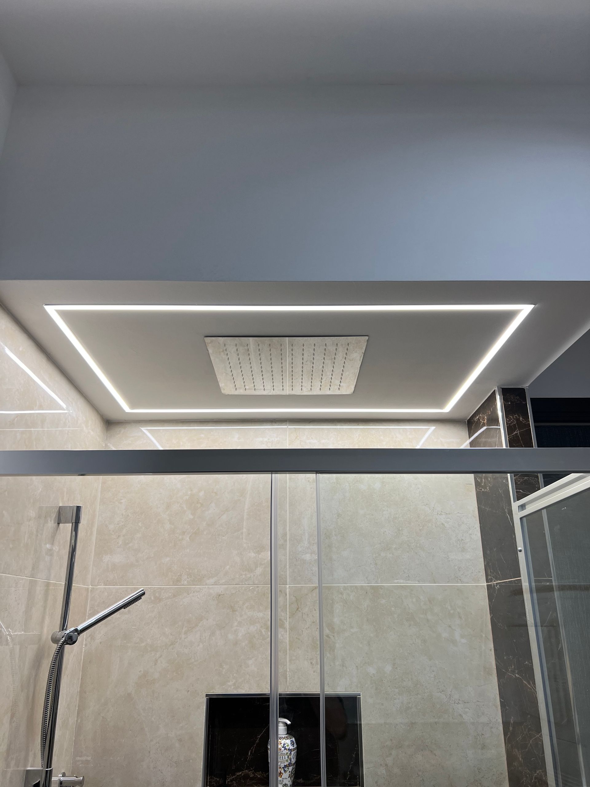 Bagno moderno con faretto quadrato da incasso nel soffitto, soffione doccia e box doccia in vetro.