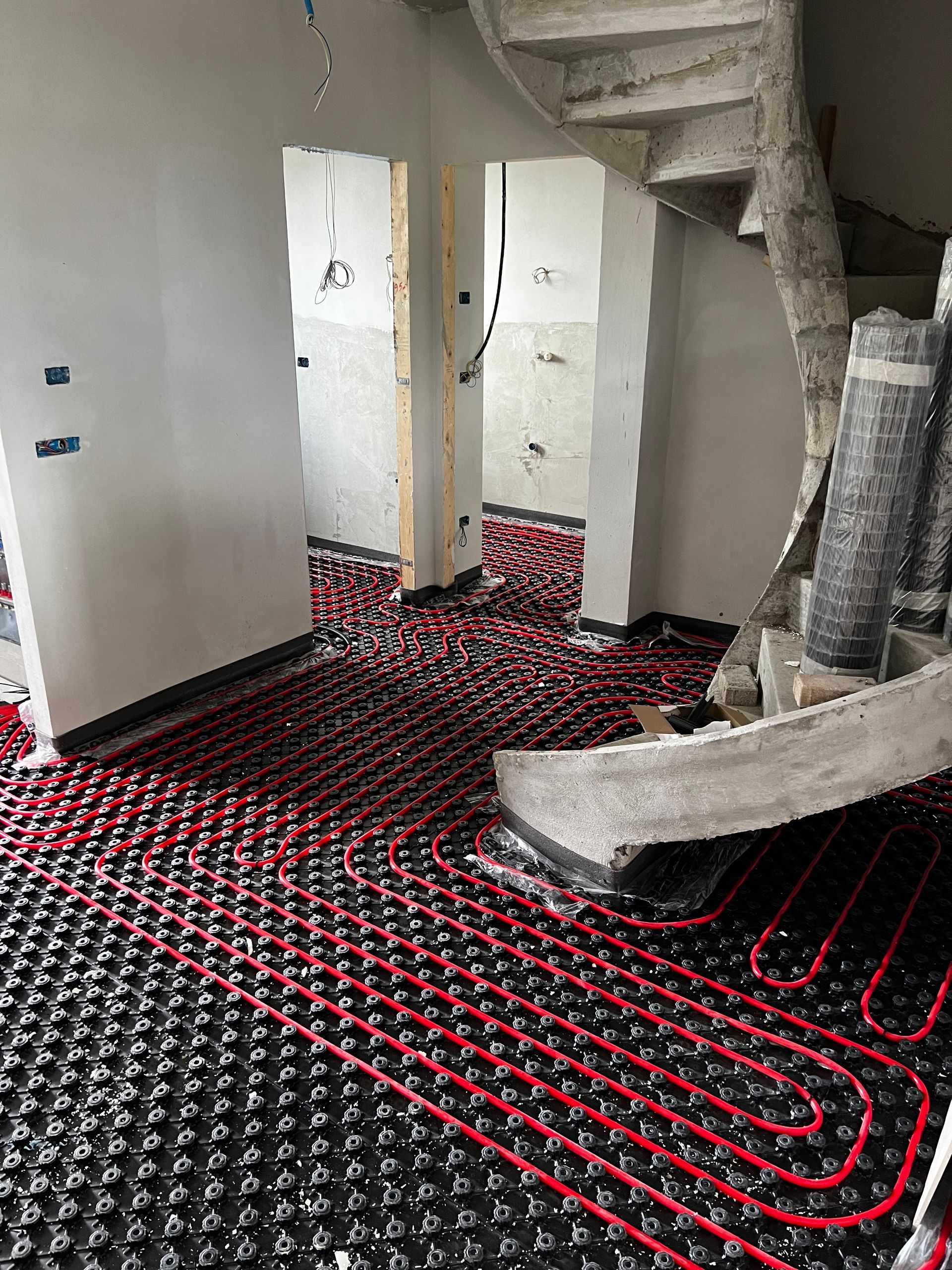 Installazione di un sistema di riscaldamento a pavimento radiante rosso e nero in una stanza con scala a chiocciola.