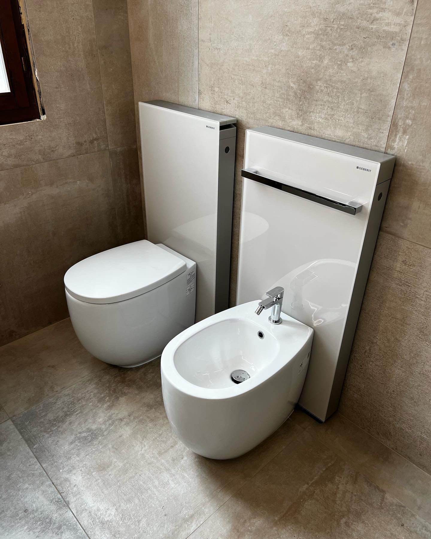 WC e bidet bianchi con impianto idraulico moderno e nascosto in un bagno piastrellato.