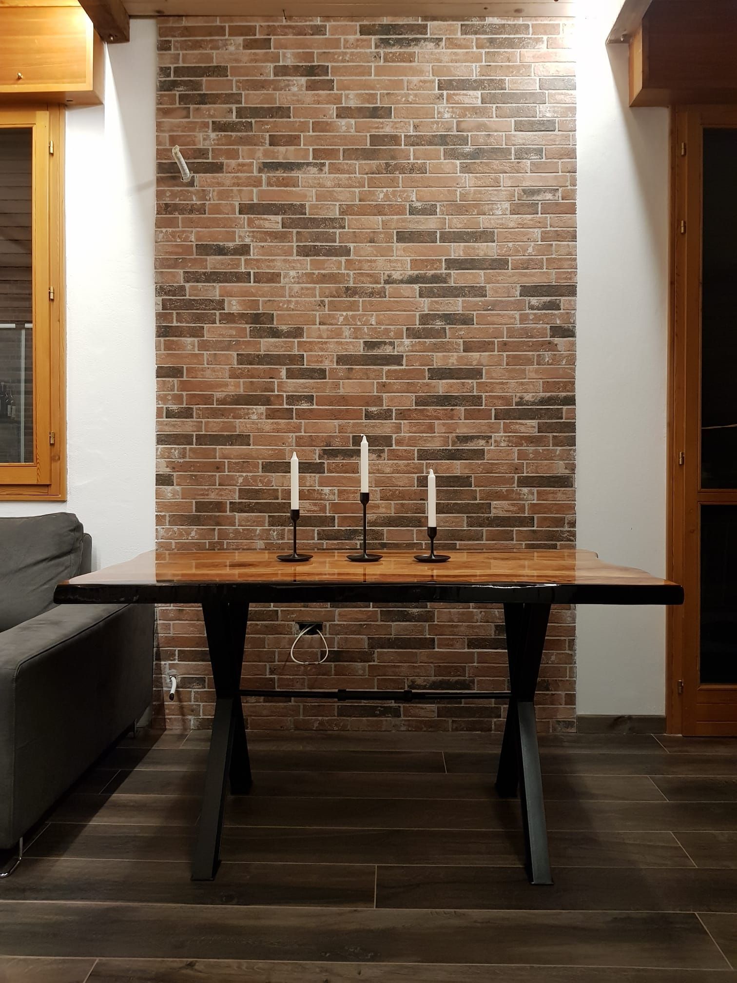 Tavolo con gambe nere, candele, davanti a un muro di mattoni e pavimento in legno.