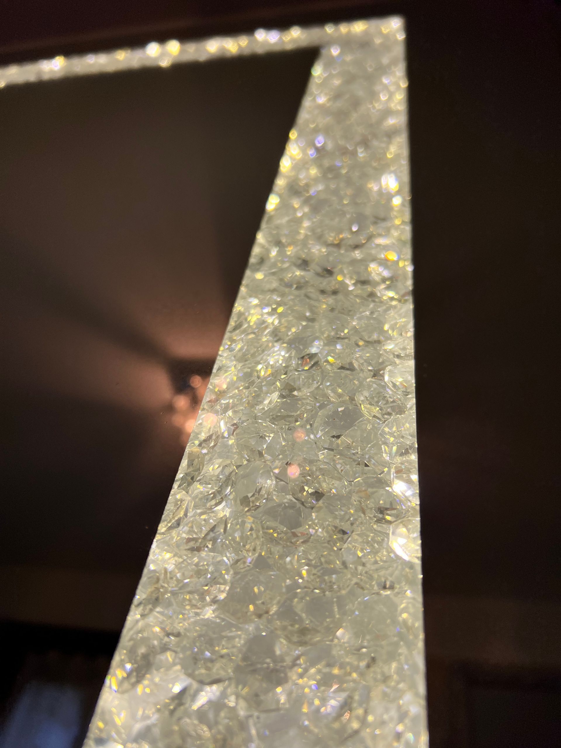 Primo piano dell'angolo di uno specchio ricoperto di cristalli scintillanti. Un lampadario si riflette nello specchio.