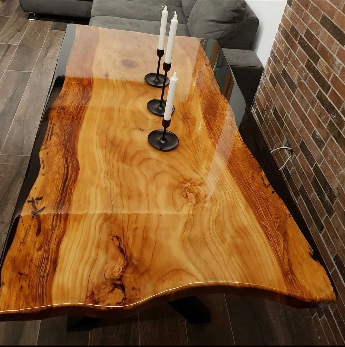 Tavolo in legno con finitura lucida, candele, posizionato in una stanza con divano e parete in mattoni.