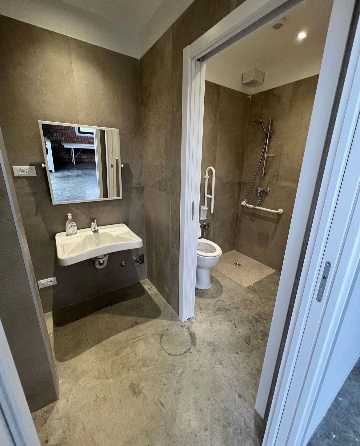 Bagno accessibile con lavandino, specchio e doccia con maniglioni.