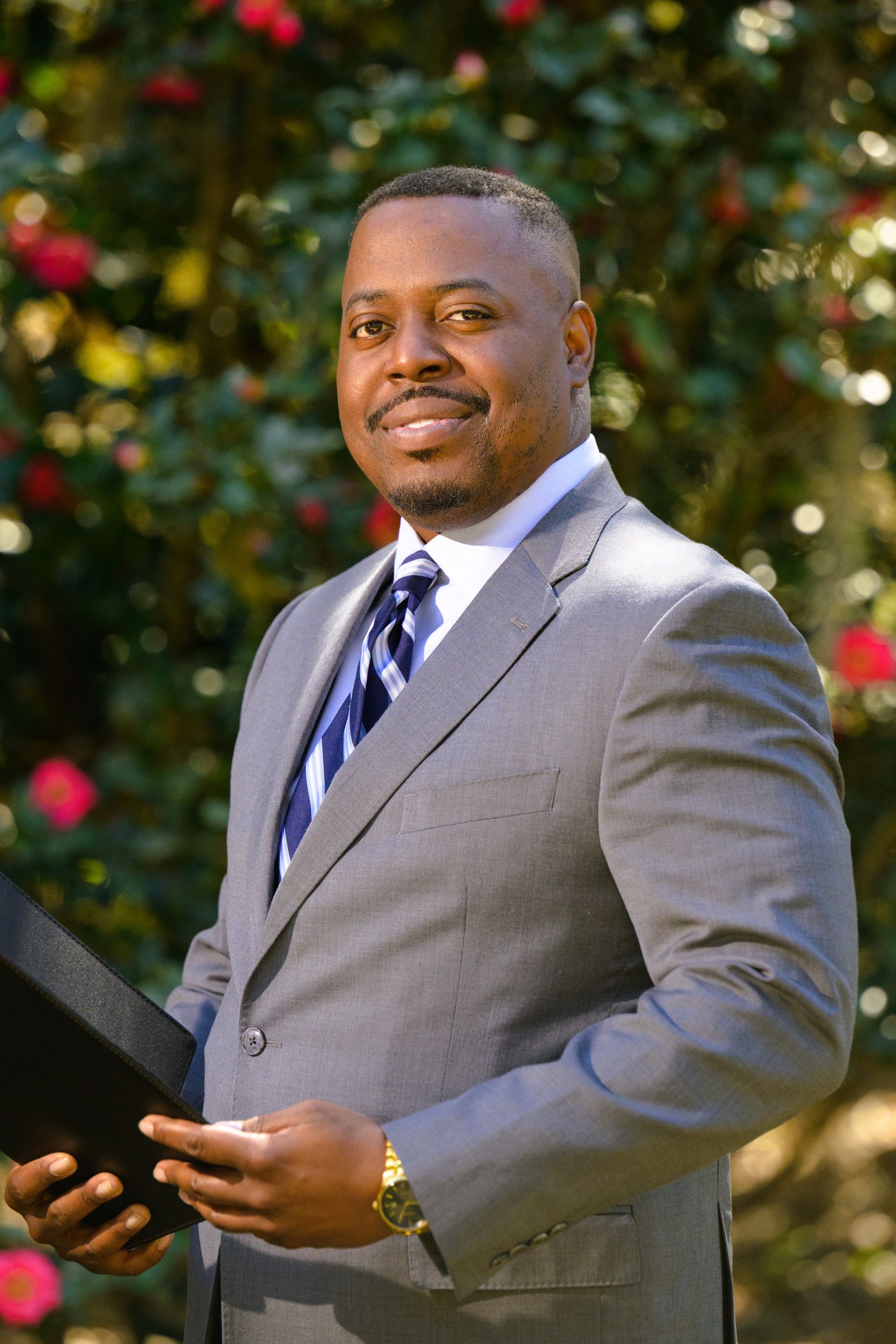 Florida Attorney Dave in a gray suit holding a court documents, with greenery and red flowers in the background.