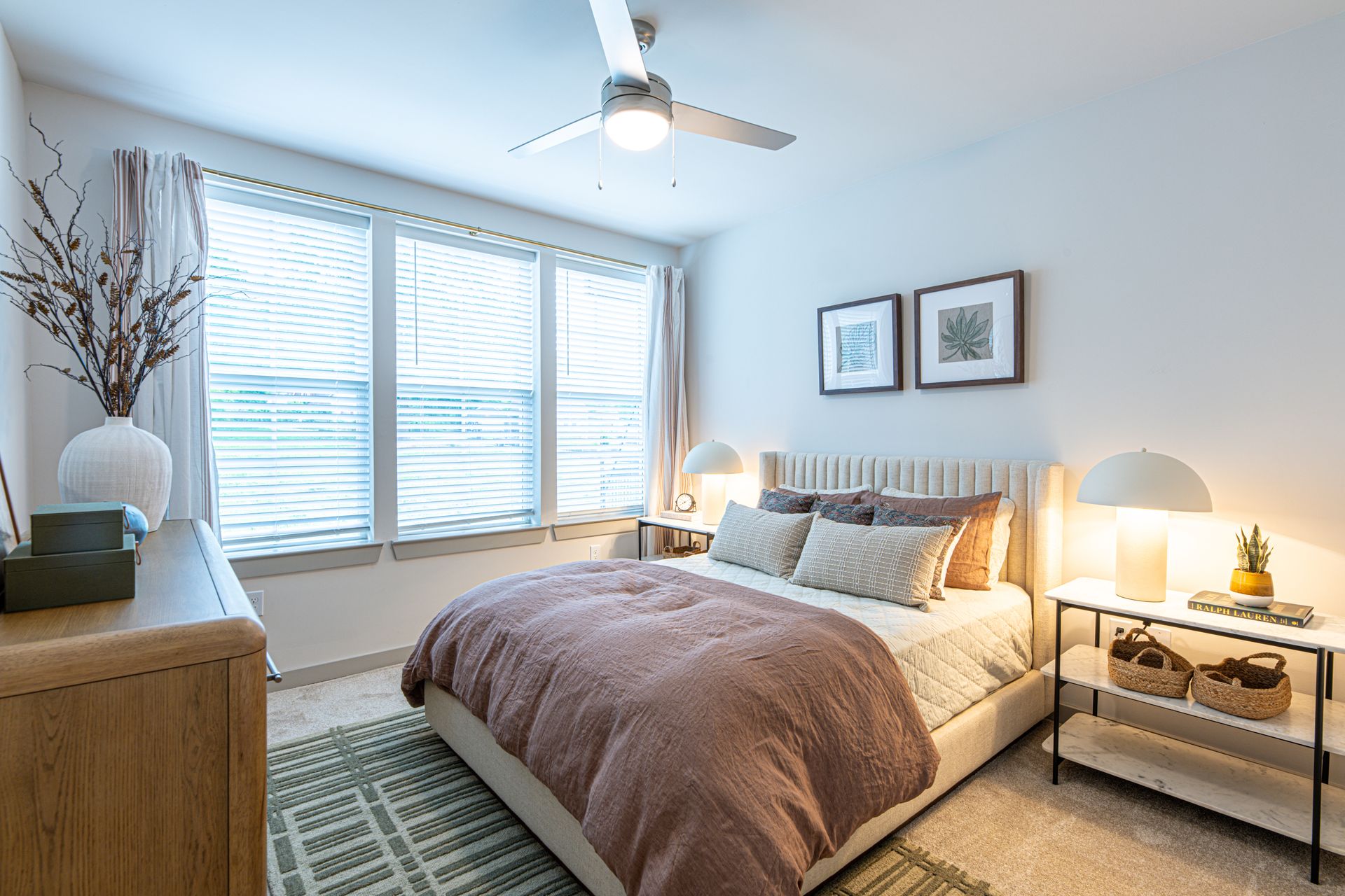 A bedroom with a king size bed , dresser , nightstand , mirrors and a ceiling fan.