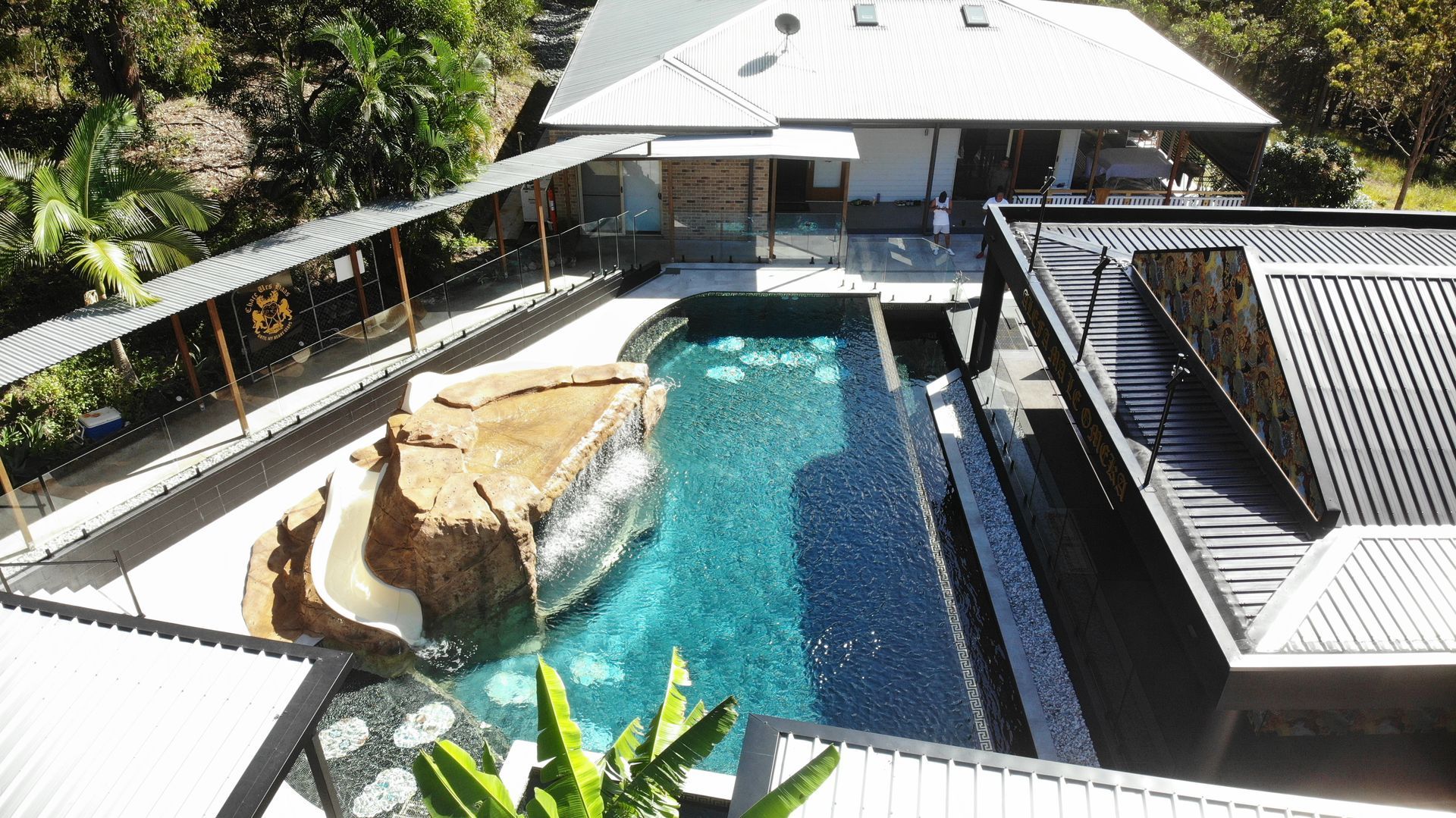 Backyard pool with a rock waterfall, blue water, and a white-roofed house beside it