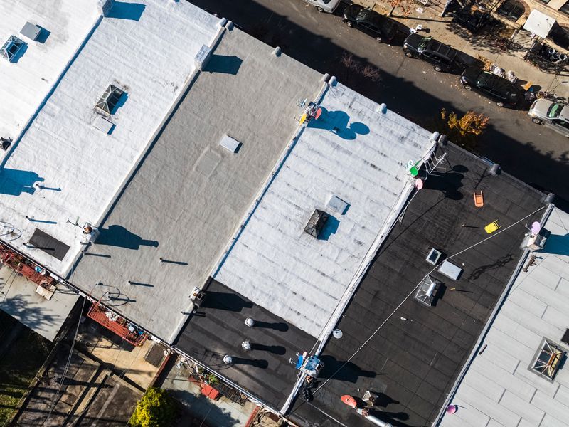 Aerial view of rooftops with workers inspecting a white roof and surrounding buildings.