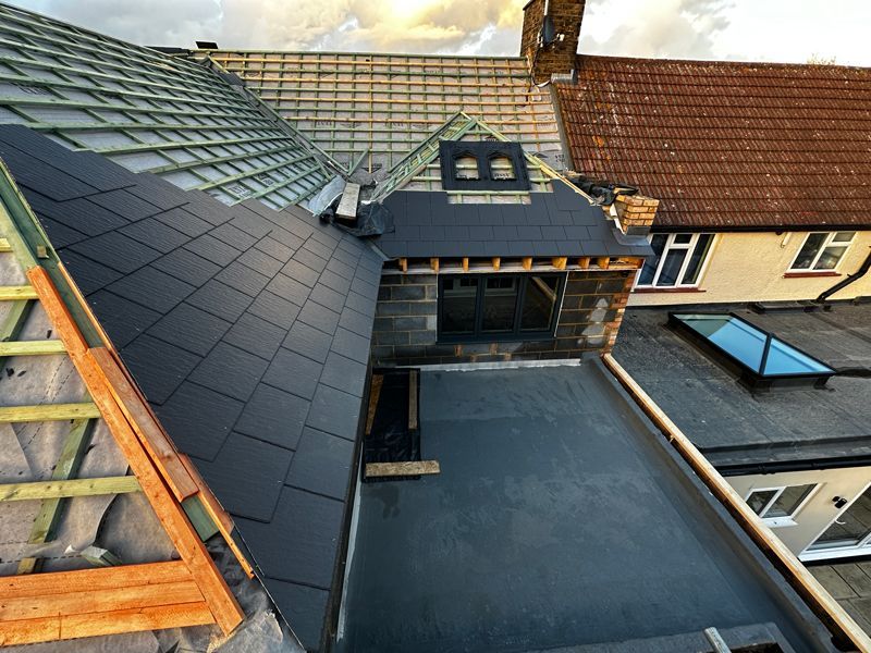 Rooftop view of black metal roofing and a dormer over a courtyard beside tiled residential houses