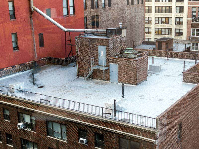Snow-covered city rooftop with brick buildings, railings, and HVAC units