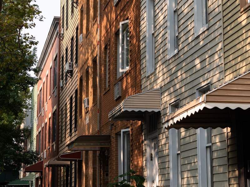 Row of brick and gray townhouses with awnings along a tree-lined street