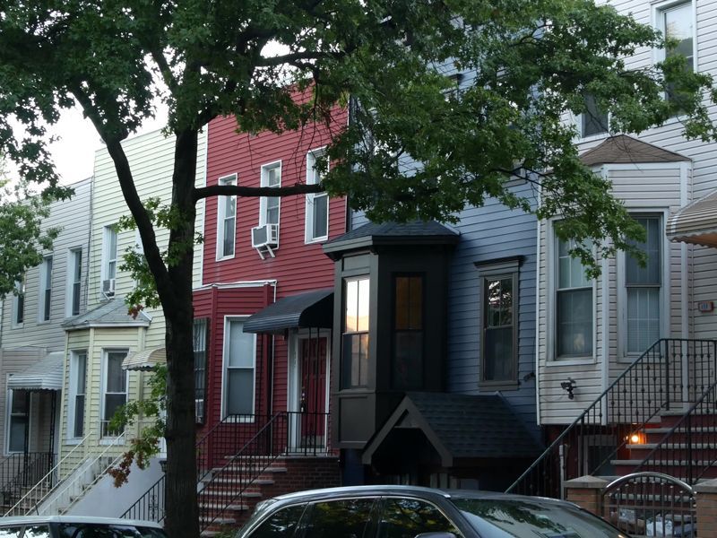 Row of colorful townhouse facades with stoops and trees lining a residential street