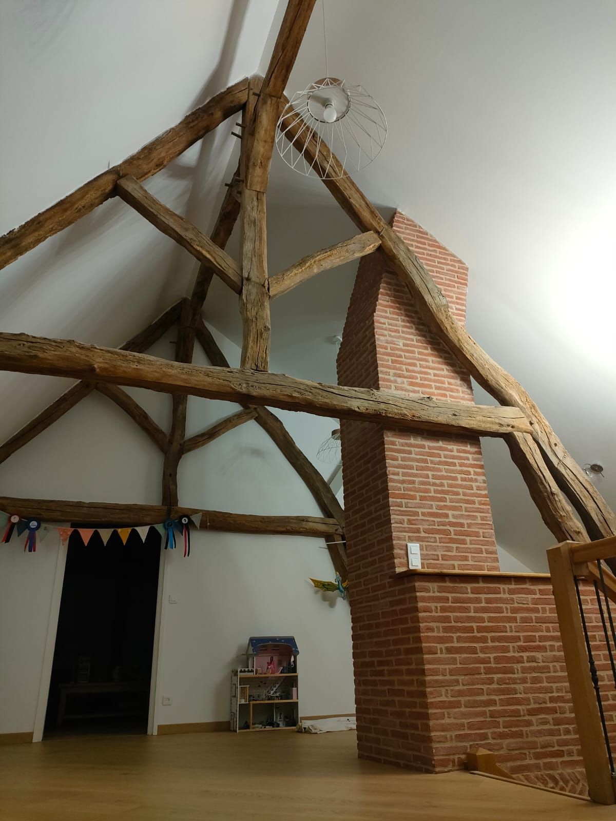 Intérieur avec poutres apparentes, cheminée en briques et porte ouverte.
