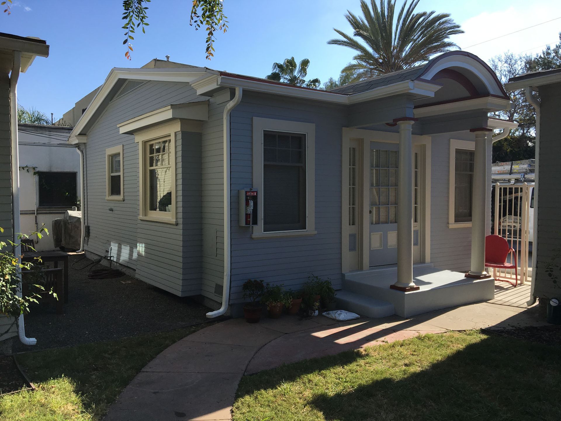Blue cottage with white trim, a small porch, and a walkway on a sunny day.