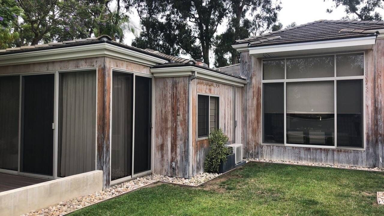 Exterior view of a weathered building with a tile roof, windows, and a small patch of grass.