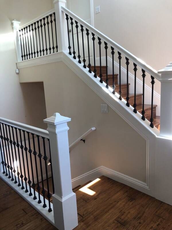 Staircase with white railing, black spindles, and wooden steps. Sunlight shines on the hardwood floor.