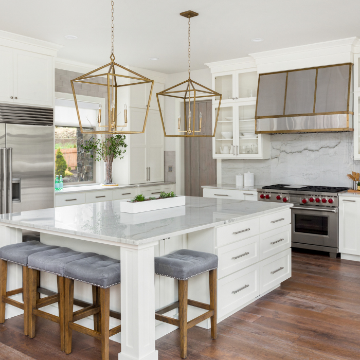 Bright, white kitchen with island, marble countertops, pendant lights, stainless steel appliances, and wood floors.