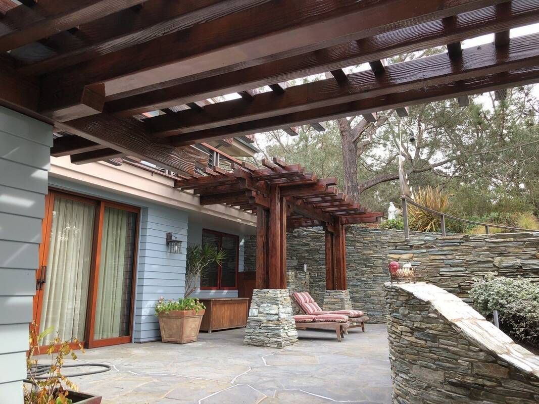 Wooden pergola over a patio, stone walls, lounge chairs.