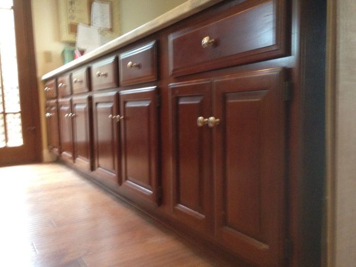Dark wood kitchen cabinets with gold hardware, below a light countertop.