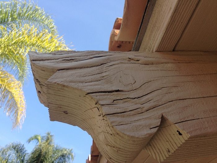 Close-up of a weathered, decorative wooden beam, part of a roof overhang, with visible grain and carvings.