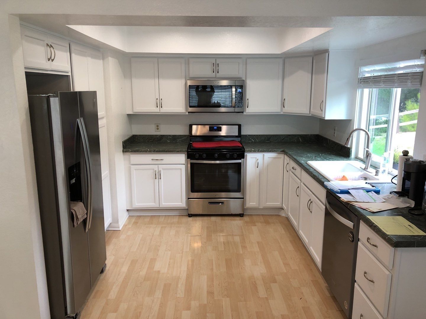 Bright, white U-shaped kitchen with stainless steel appliances, green countertops, and light wood flooring.