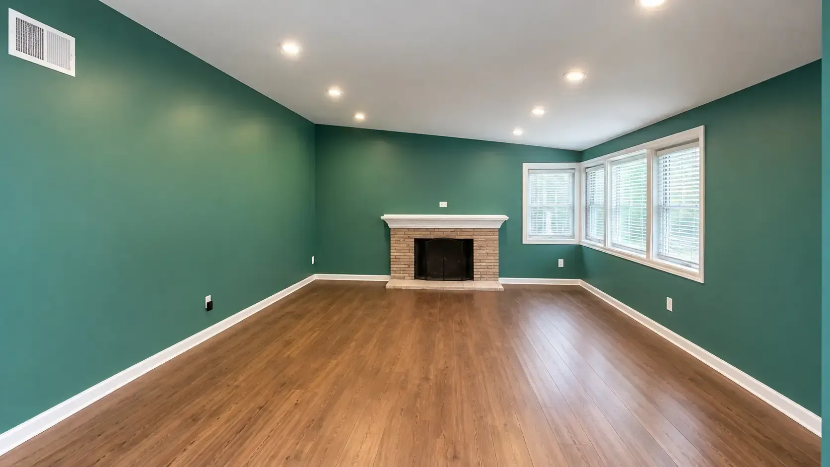 Green-walled living room with a fireplace, hardwood floors, and recessed lighting.