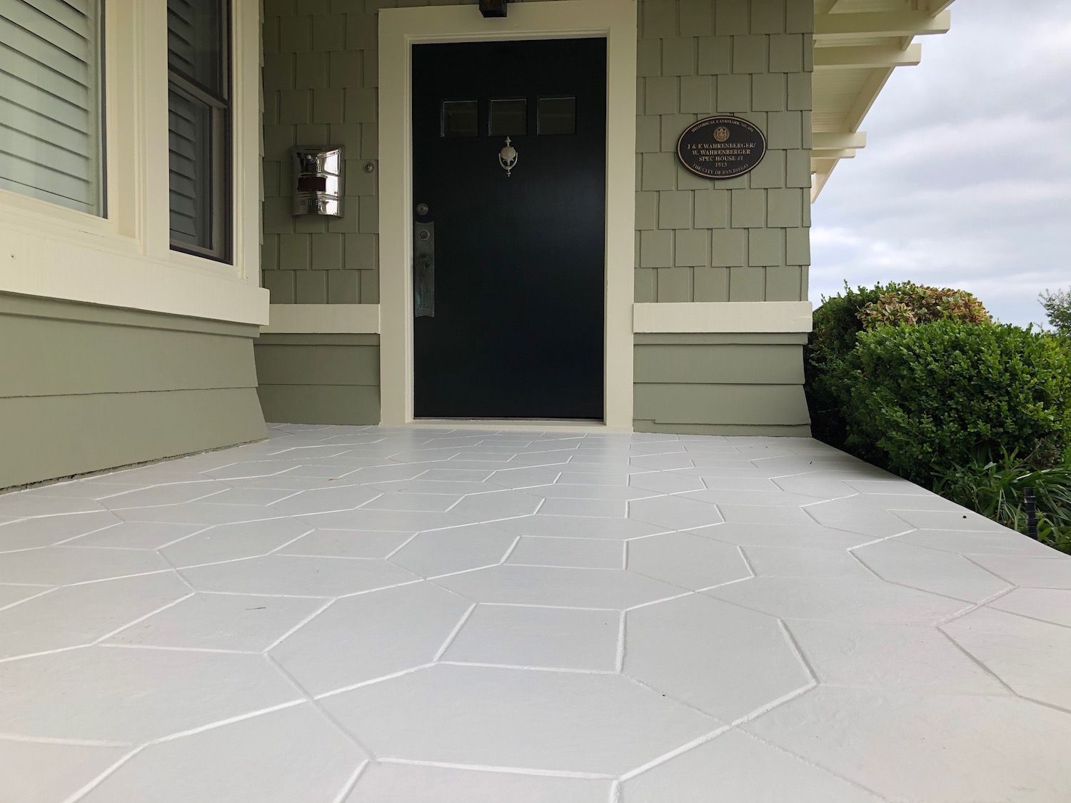 Gray-painted front porch with patterned surface leading to a dark green door under an overcast sky.