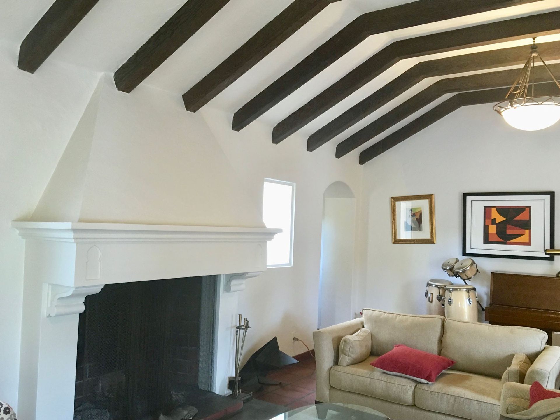 Living room with fireplace, white walls, dark wooden beams, sofa, artwork, and arched doorway.