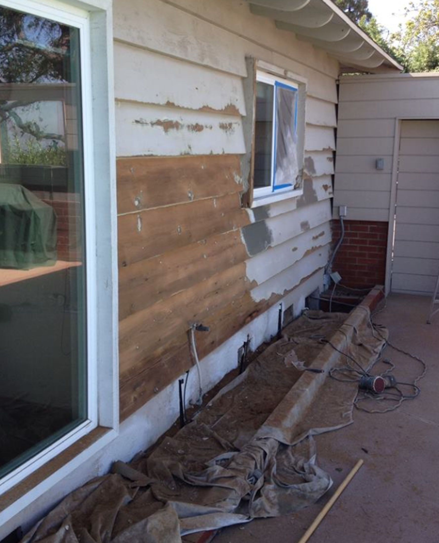 Exterior wall of house under renovation; old siding removed, revealing wooden underlayment.