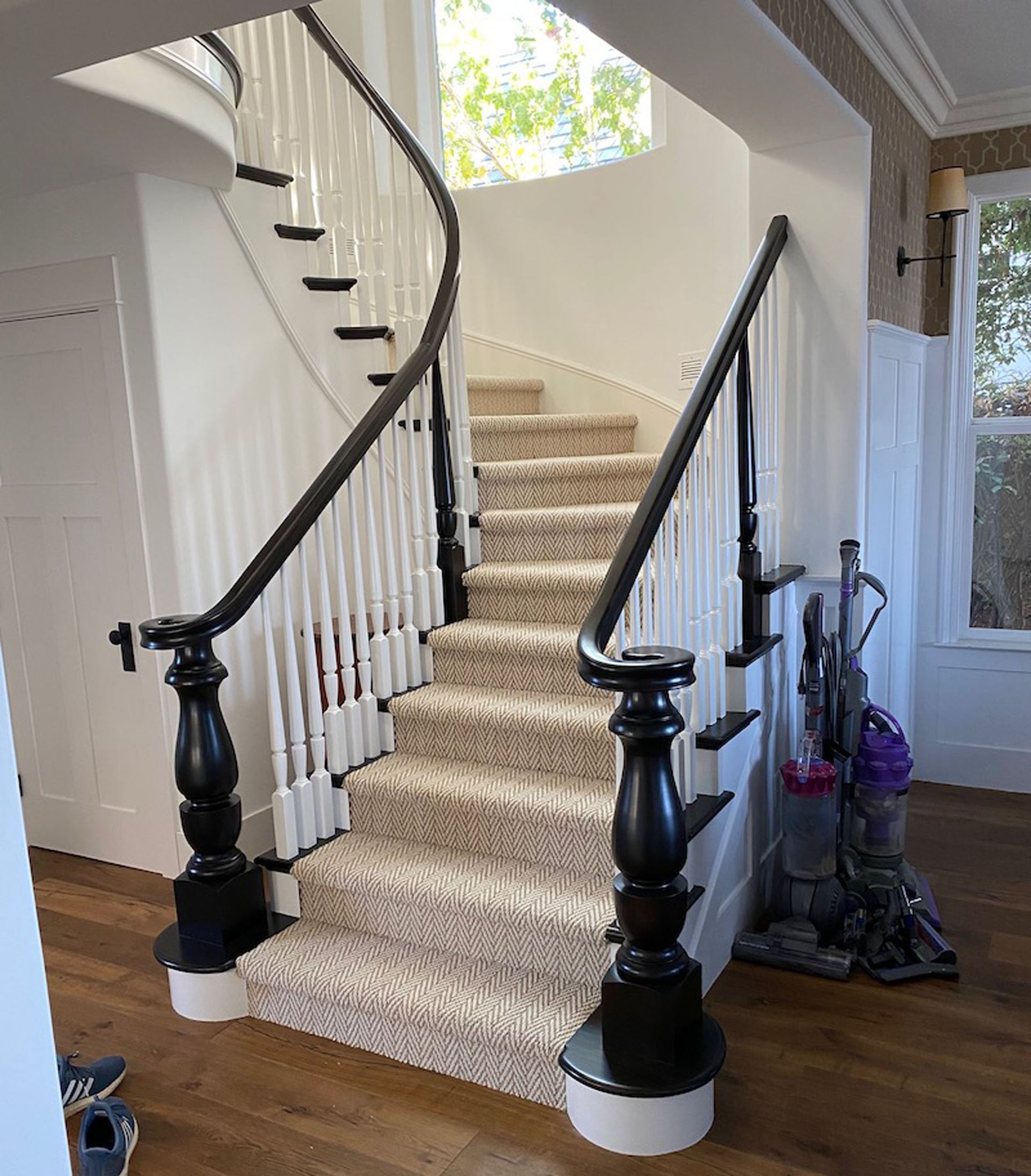 Curved staircase with carpeted steps, white balusters, and black handrails in a light-filled home.