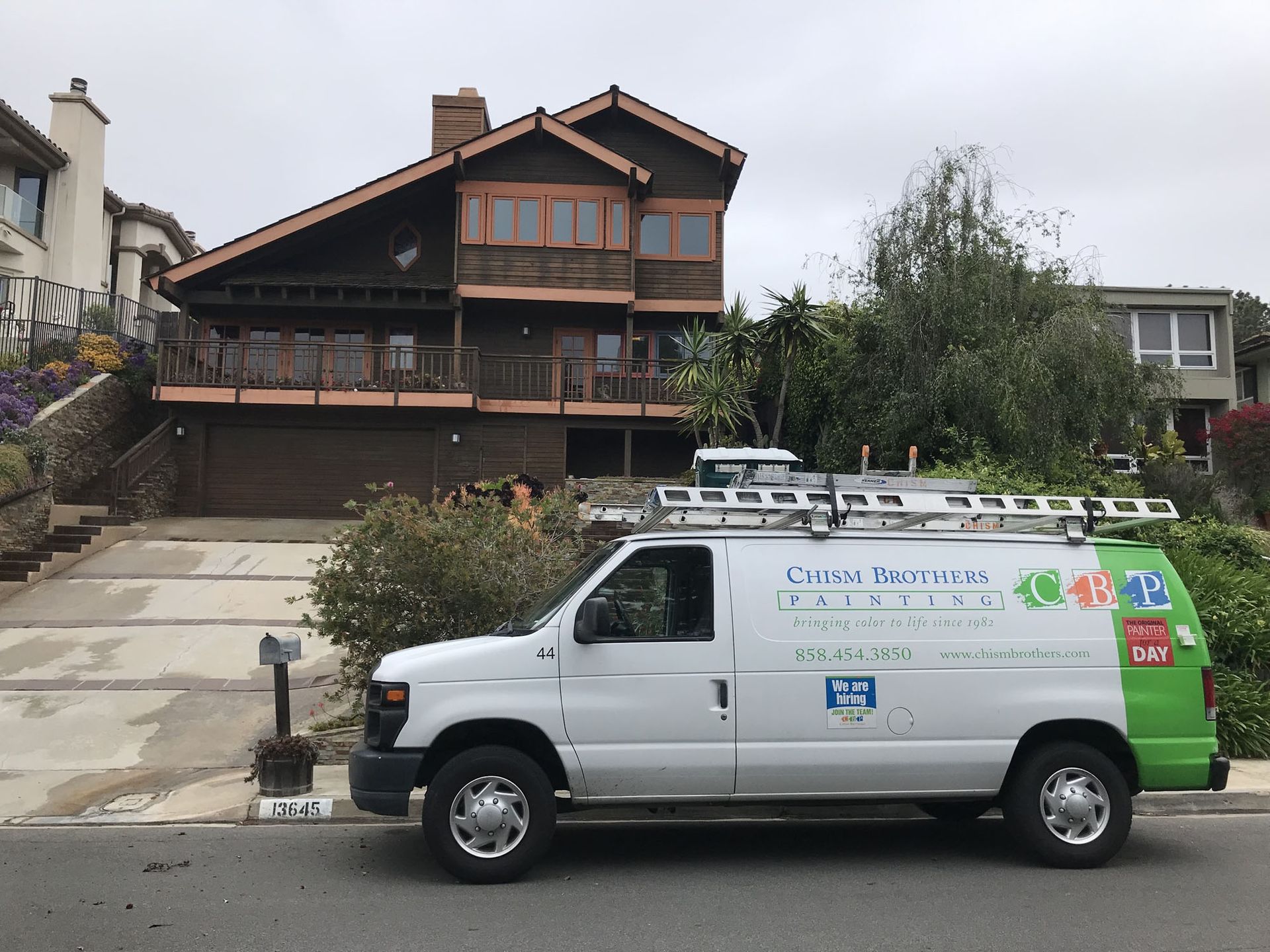 White van with a ladder parked in front of a two-story house.