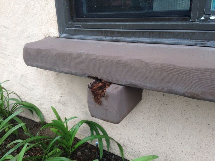 Window ledge with brown support block, damaged area, set in light beige wall, with green plants.