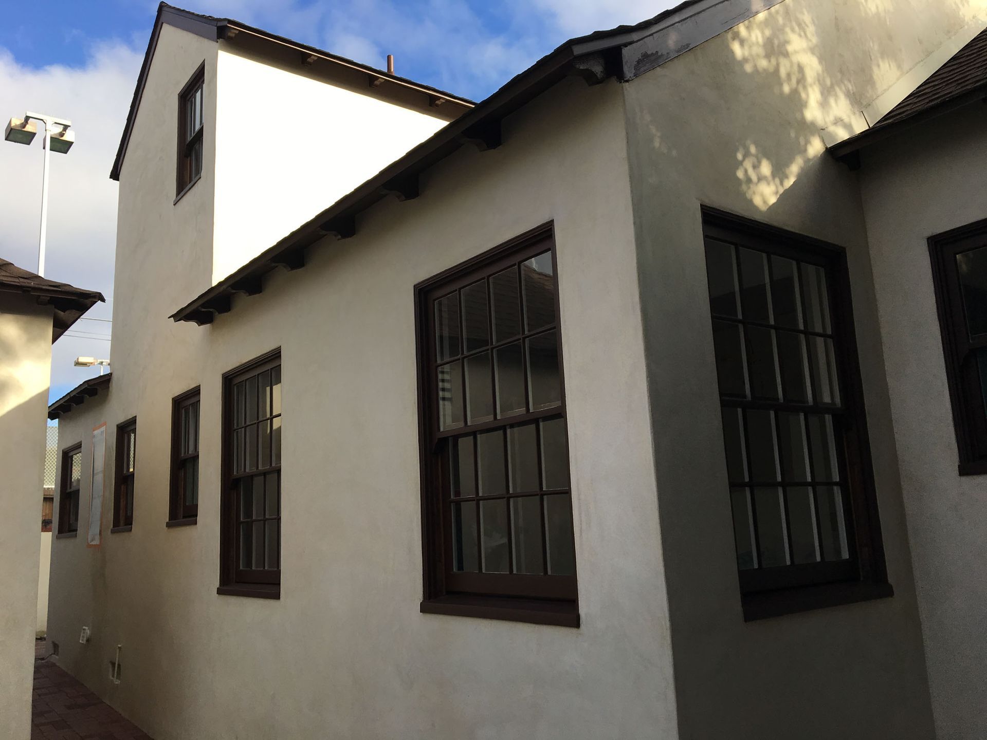 White stucco building with brown-framed windows, against a blue sky.