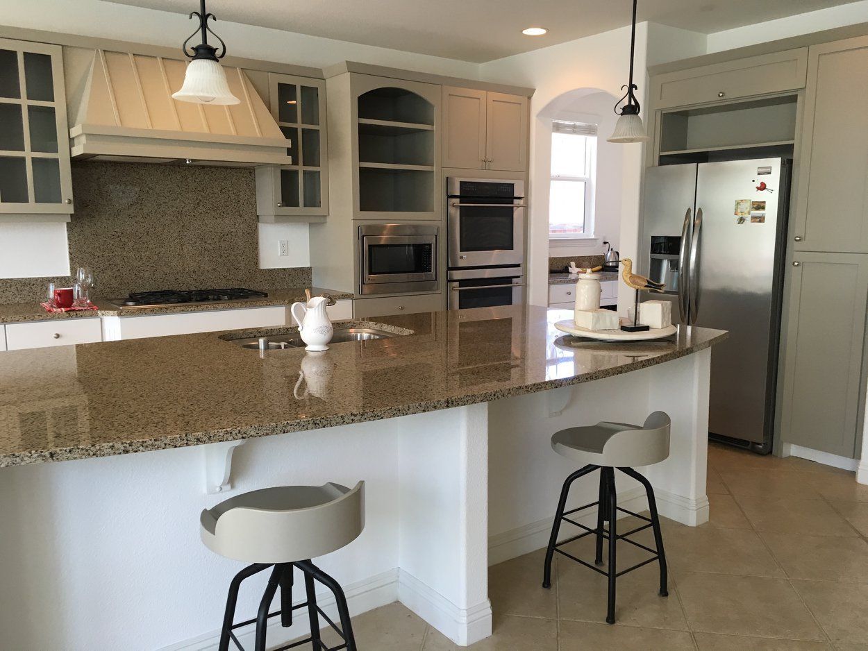 Kitchen with granite countertops, light-colored cabinets, stainless steel appliances, and bar stools.