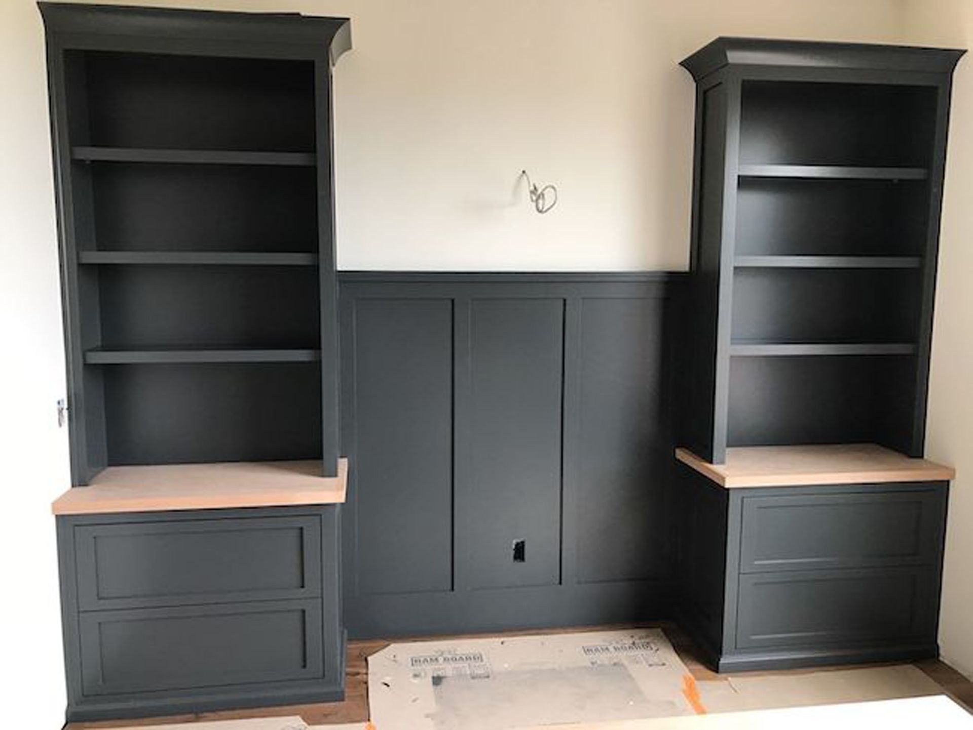Dark gray built-in bookshelves with wood countertops flank paneled wall. Room is under construction.