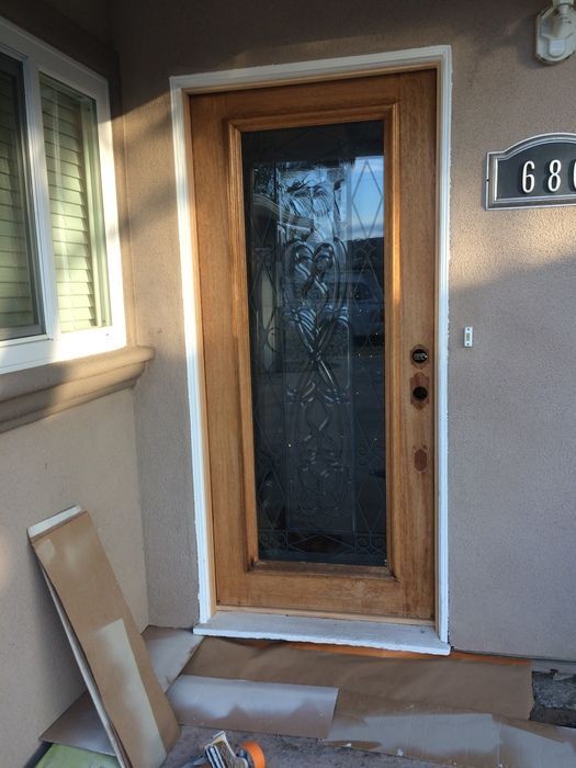 Wooden front door with glass panel, white trim, and a house number on the side.