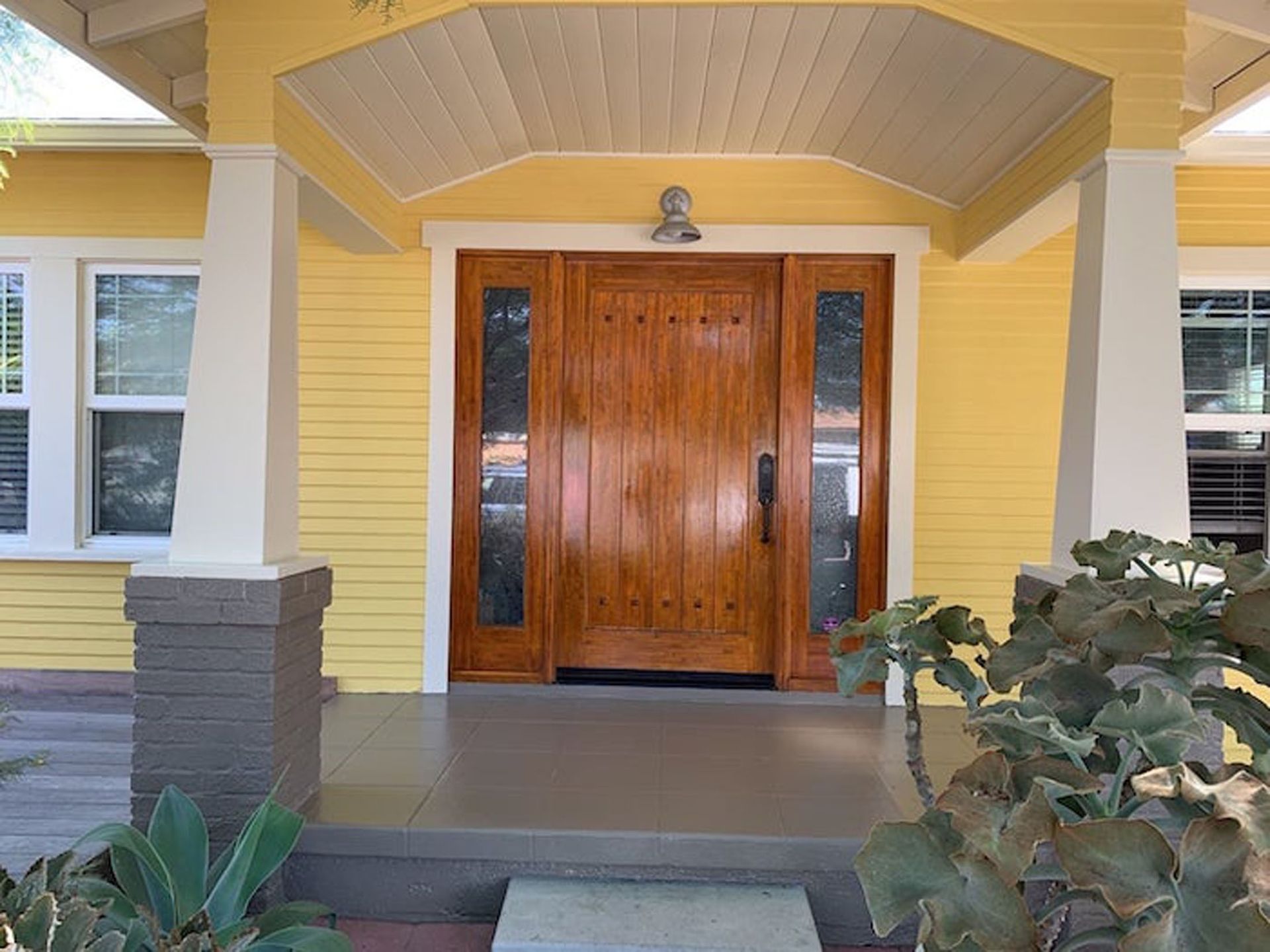 Yellow house with wooden front door, sidelights, and porch columns.