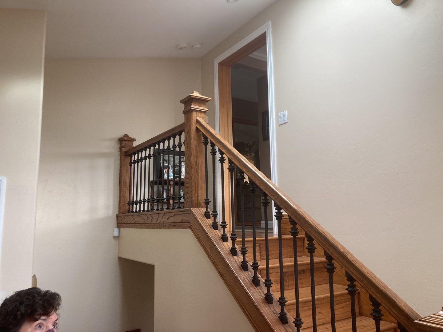 Staircase with wooden banister and black spindles, leading to a door; beige walls.