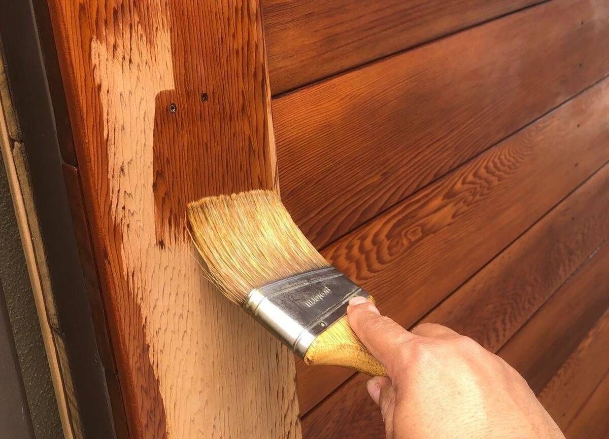 Person applying stain to wooden boards with a paintbrush.