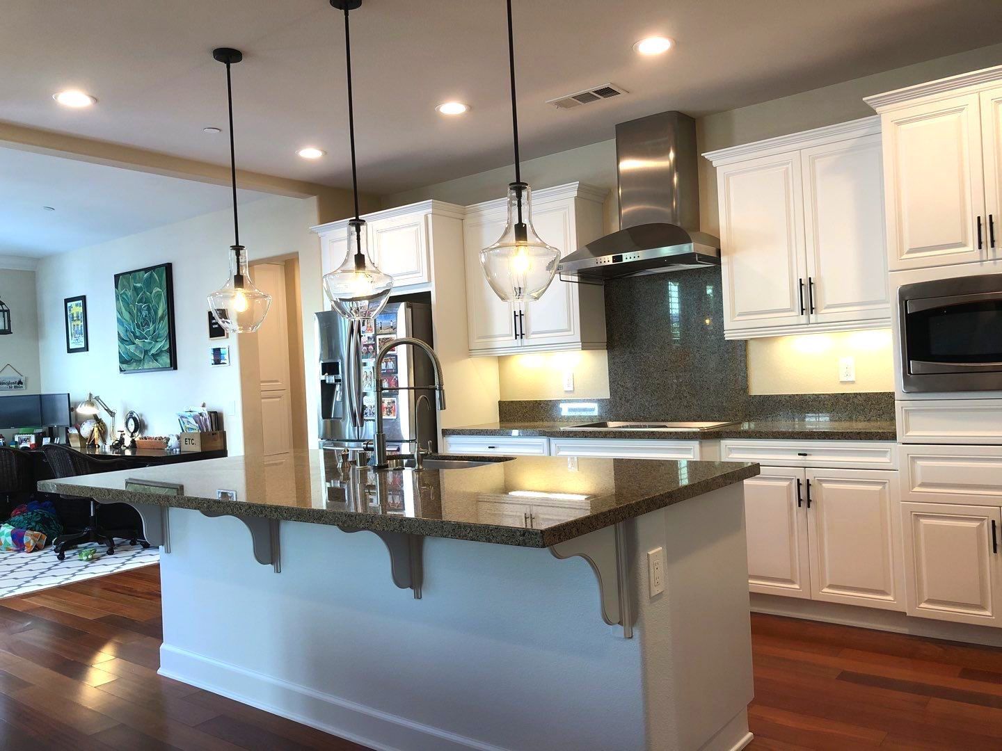 Kitchen with white cabinets, dark granite countertops, and pendant lights over the island.