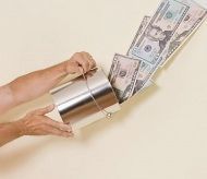 Person's hand holds a silver metal can, money flowing out. Bills include $50 and appear to be falling.