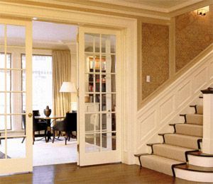 Elegant interior with French doors, stairway, and a room with a table, chair, and a lamp.