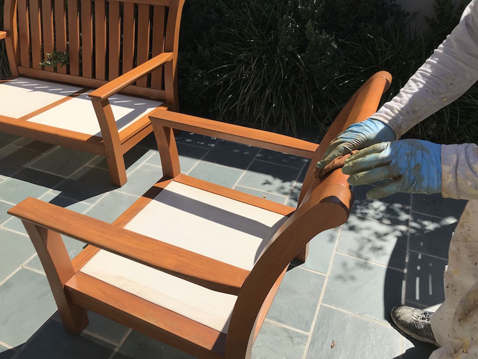 Person wearing gloves staining wooden outdoor furniture.