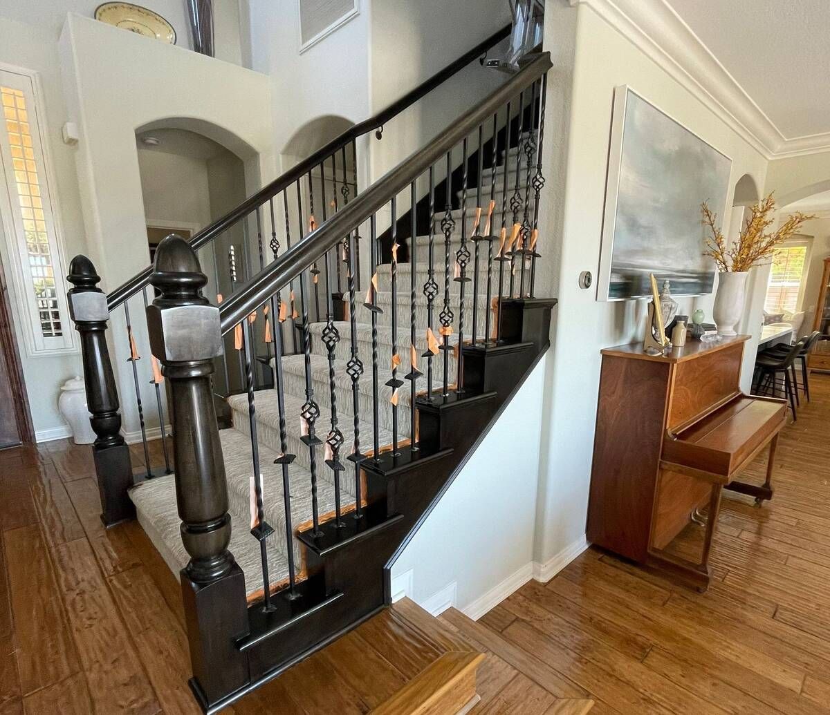Wooden staircase with wrought iron balusters, leading upstairs, next to a piano.