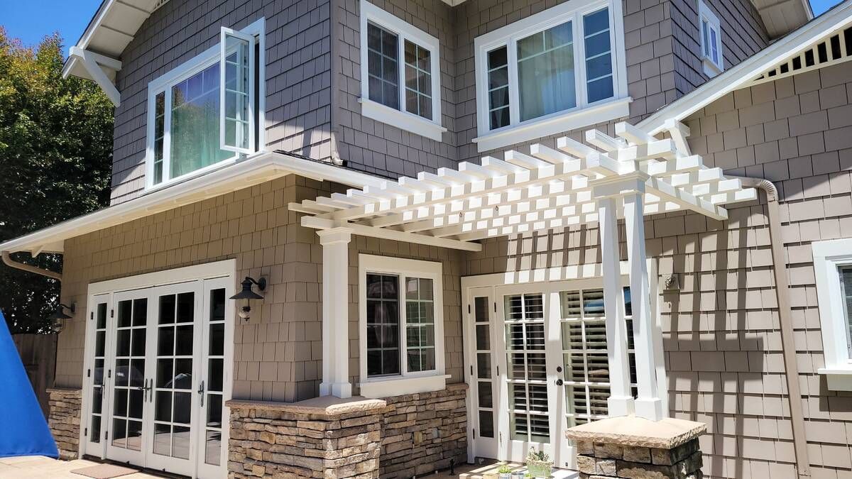 House exterior with a white pergola, French doors, and gray siding.