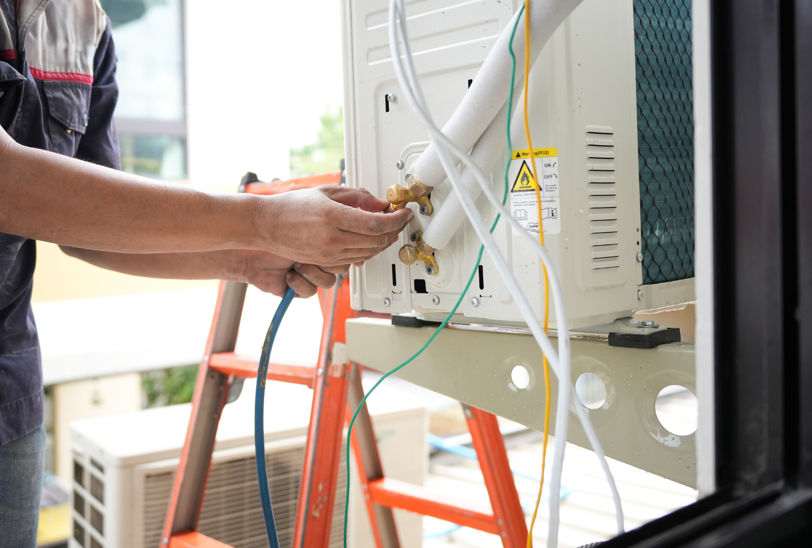 Technician connecting wires to an outdoor air conditioner unit with a ladder nearby