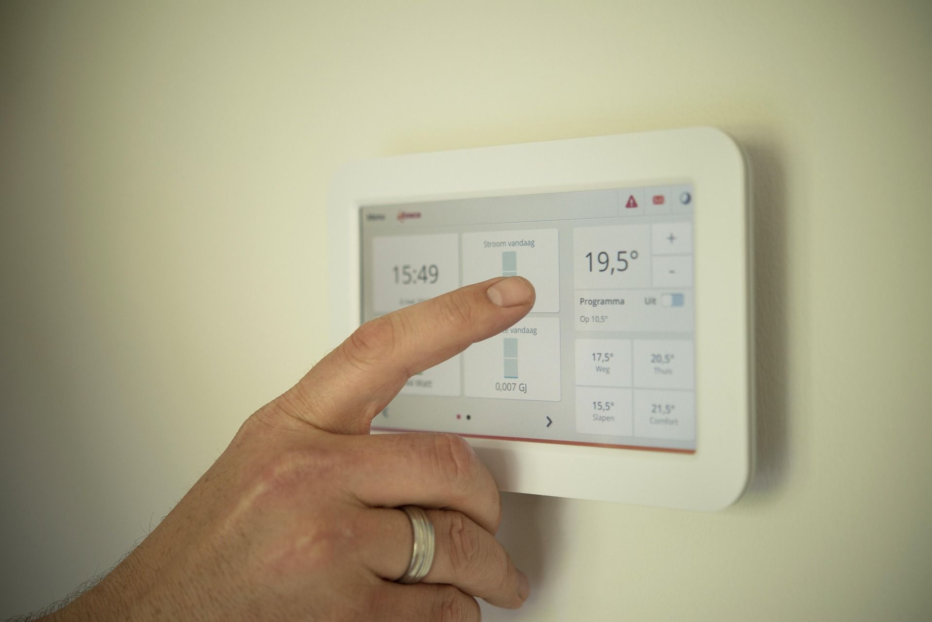 Hand adjusting a white wall thermostat touchscreen showing temperature settings