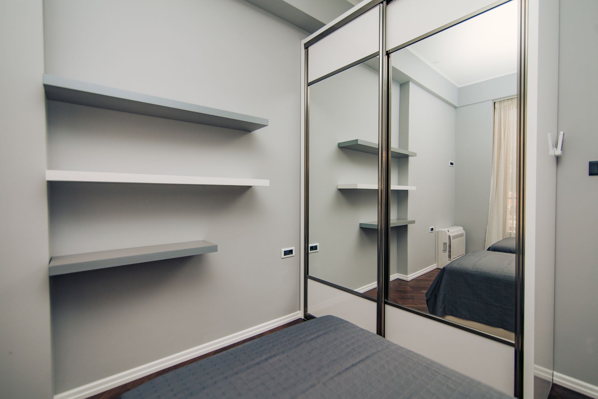 A bedroom with gray walls, a bed, a mirrored closet, and shelves.