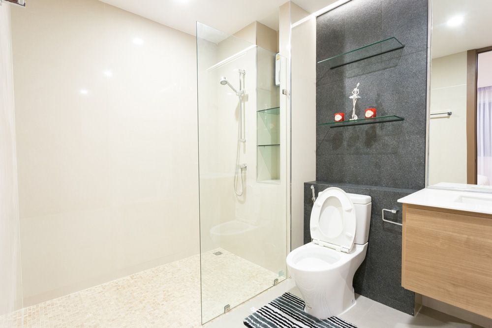 Modern bathroom with a glass shower, toilet, and vanity with a dark accent wall and shelves.