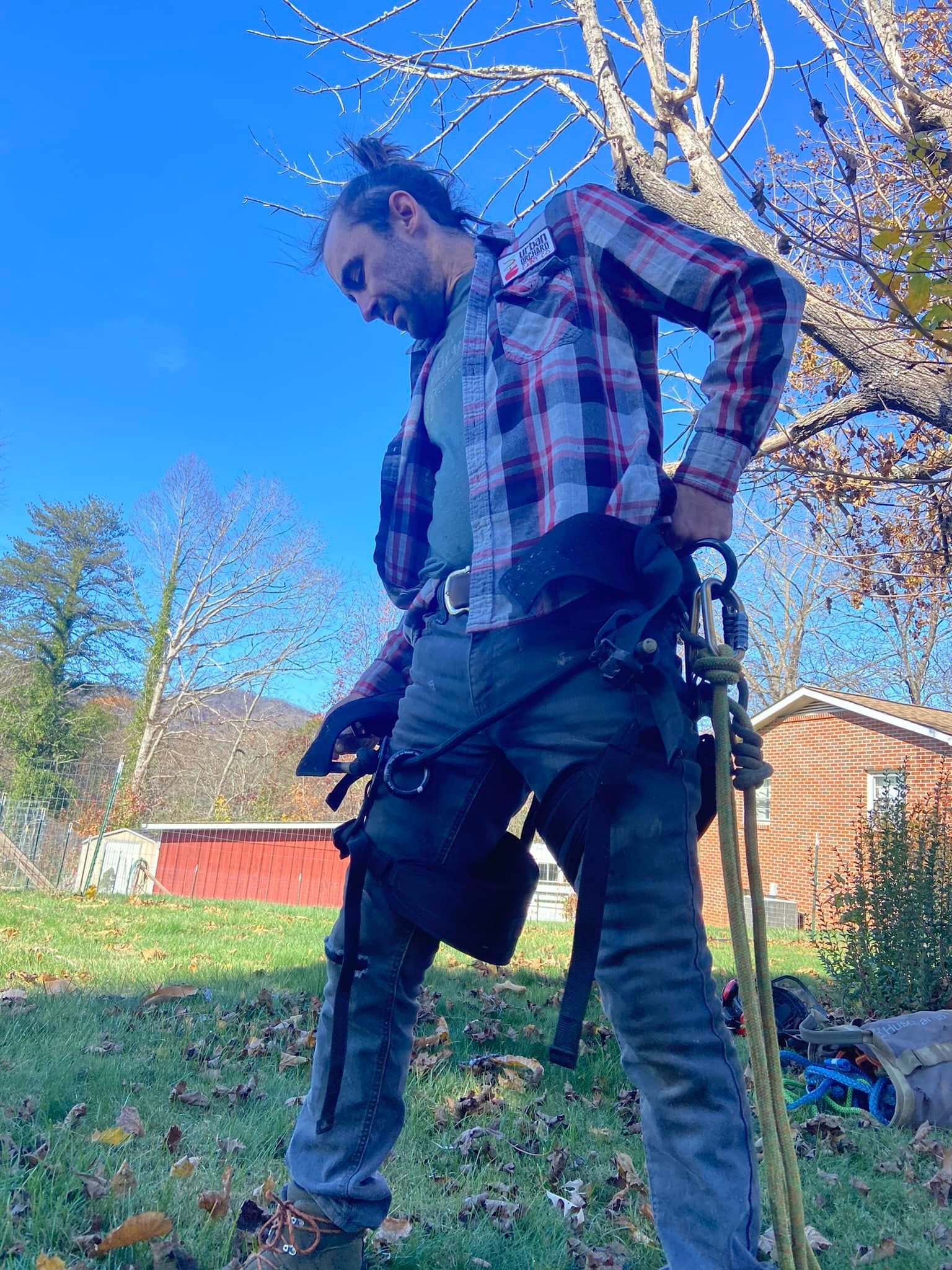 Person outdoors in a plaid shirt adjusting a harness beside a brick house on a sunny day