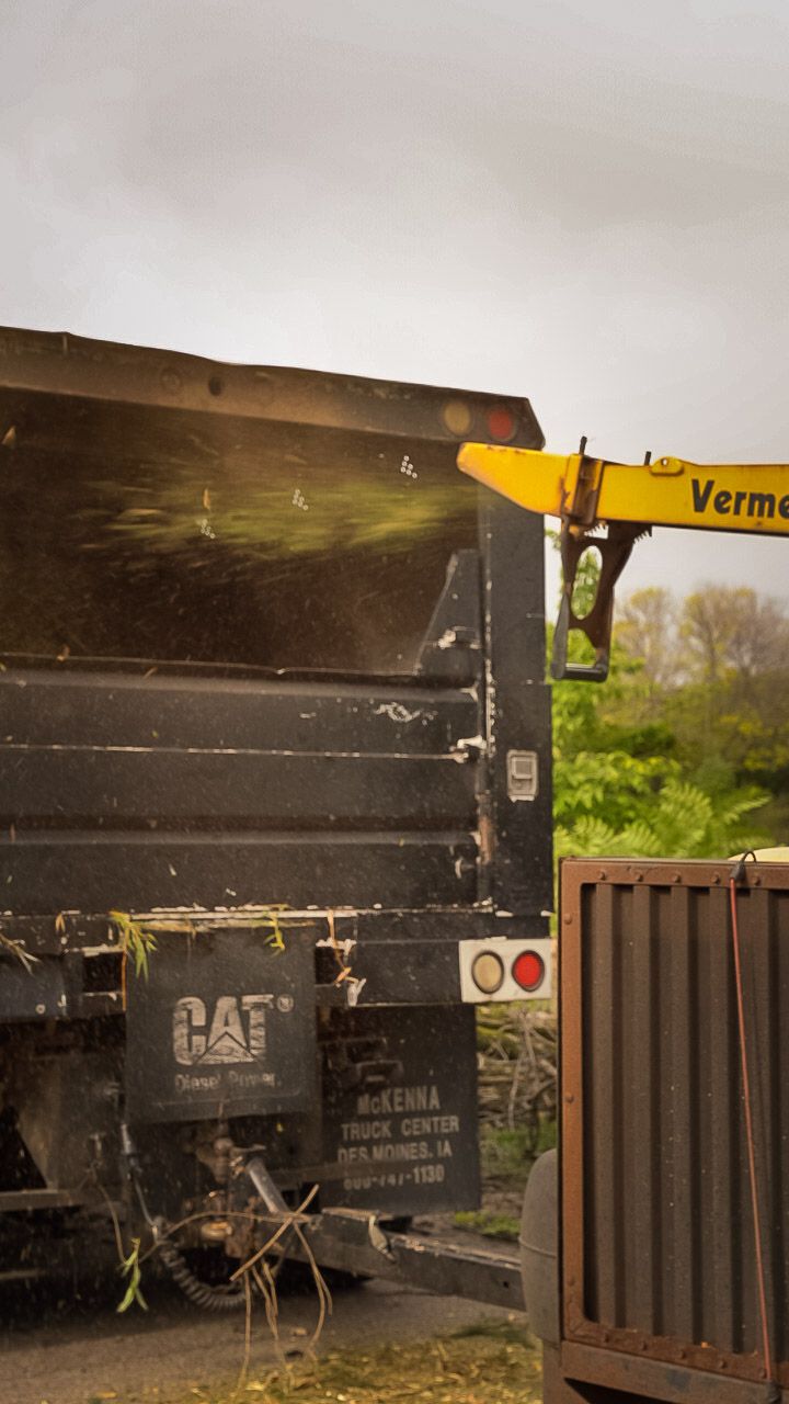 Yellow crane lifts a black dump truck bed at a construction site.